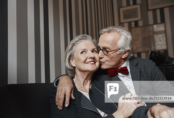 Senior Mann  der seine Frau auf der Couch küsst.
