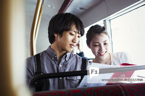 Young Japanese man and woman enjoying a day out in London  riding on a double decker bus.
