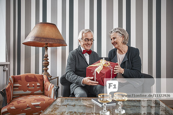Glückliches Seniorenpaar sitzend auf der Couch mit Geschenk