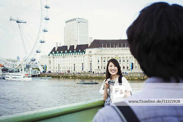 Ein junger Japaner und eine junge Japanerin genießen einen Tag in London und stehen an der Themse  im Hintergrund das London Eye.