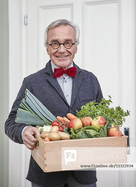 Portrait of smiling senior man holding box with produce