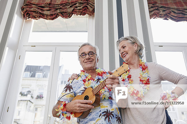 Glückliches Seniorenpaar mit Mann in hawaiianischem Hemd beim Ukulelele spielen