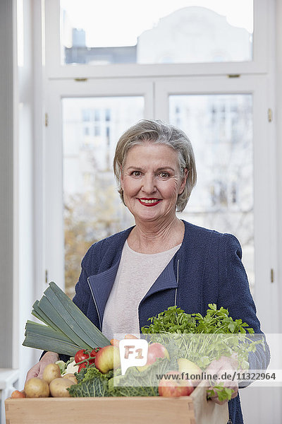 Portrait of smiling senior woman holding box with produce
