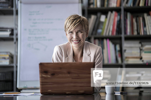 Portrait der lächelnden Geschäftsfrau mit Laptop im modernen Konferenzraum
