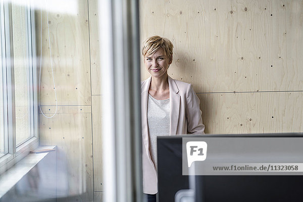 Smiling businesswoman at wooden wall in office