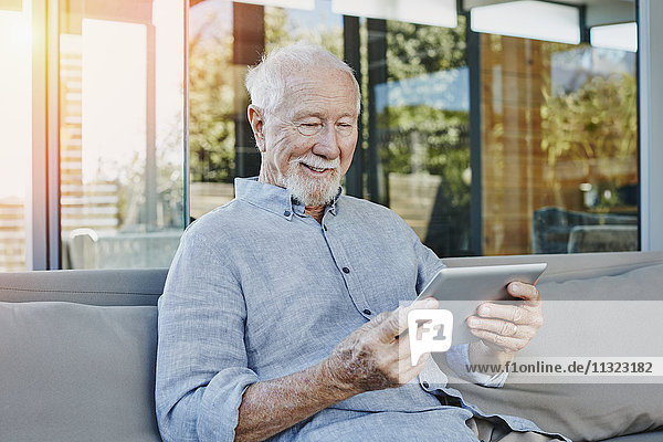 Senior Mann sitzt auf der Terrasse und liest ebook