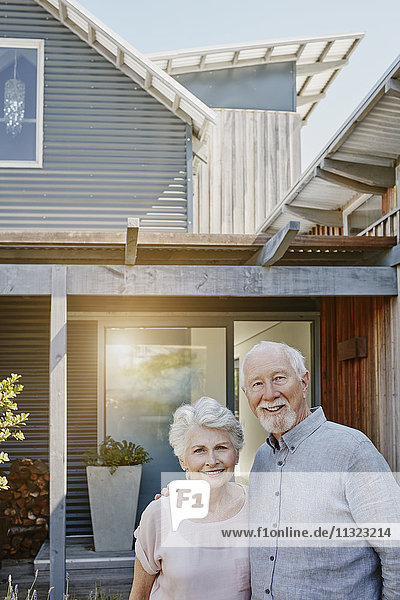 Seniorenpaar steht vor ihrem Haus und sieht zuversichtlich aus.