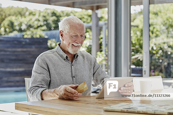 Senior Mann sitzt auf der Terrasse und bezahlt online mit Kreditkarte.