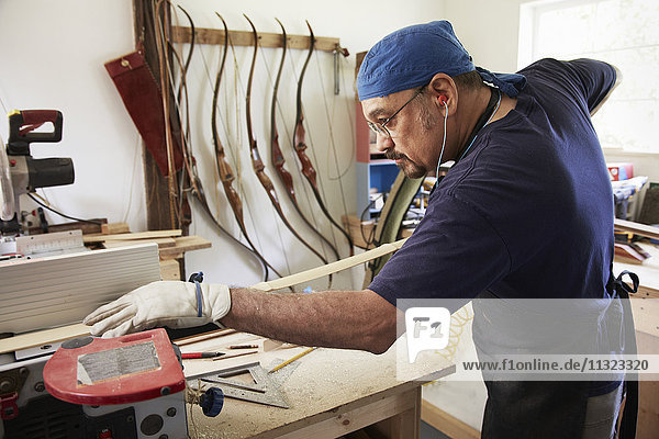 A bow maker working on a wooden bow in his workshop.