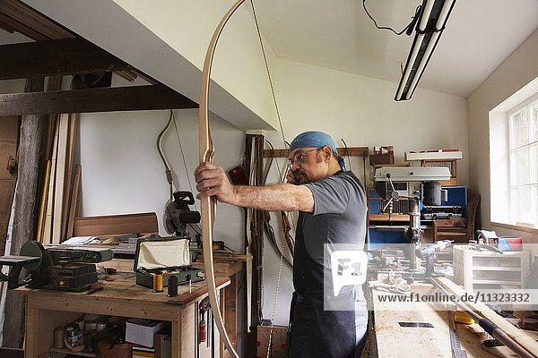 Ein Mann testet einen handgefertigten Bogen  indem er an der Bogensehne zieht.