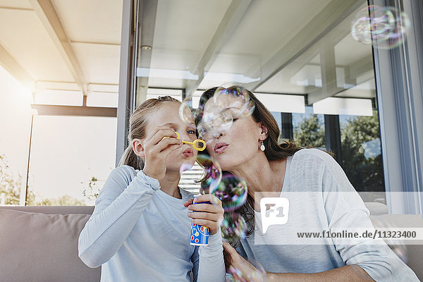 Mutter und Tochter blasen Seifenblasen auf der Terrasse