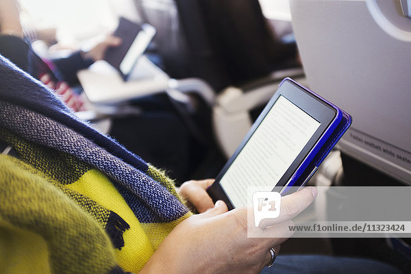 Ein Passagier in einem Flugzeug  der ein digitales Tablett benutzt.