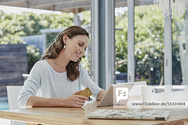 Frau sitzt auf der Terrasse und bezahlt online mit Kreditkarte.