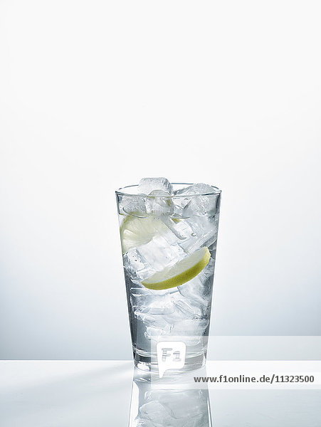 Glas mit Mineralwasser  Eiswürfeln und Zitronenscheiben vor weißem Hintergrund