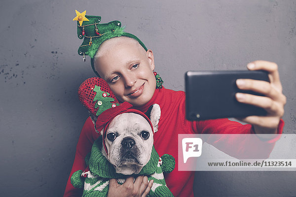 Woman with French bulldog taking selfie with smartphone at Christmas time
