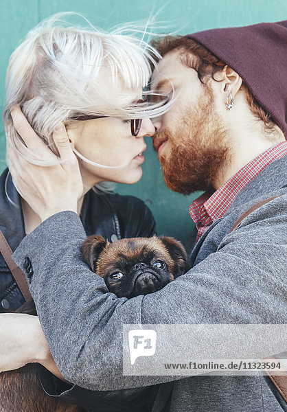Ein junges verliebtes Paar  das sich mit einem Hund küsst.