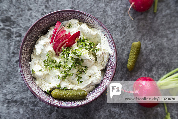 Bowl of cream cheese with herbs garnished with red radish  gherkins and cress