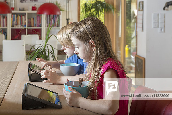 Boy and girl using tablets at breakfast table