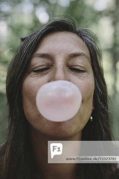 Porträt einer Frau mittleren Alters beim Blasen einer Kaugummiblase