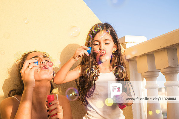 Teenage girl and her little sister blowing soap bubbles on balcony