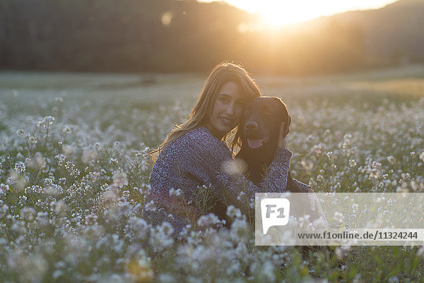 Junge Frau und ihr Hund im Blumenfeld in der Dämmerung