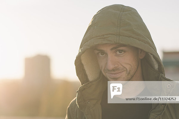 Porträt eines lächelnden Mannes mit Kapuzenjacke im Freien bei Sonnenuntergang