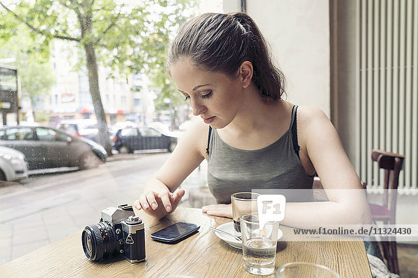 Young woman in a cafe with camera checking cell phone