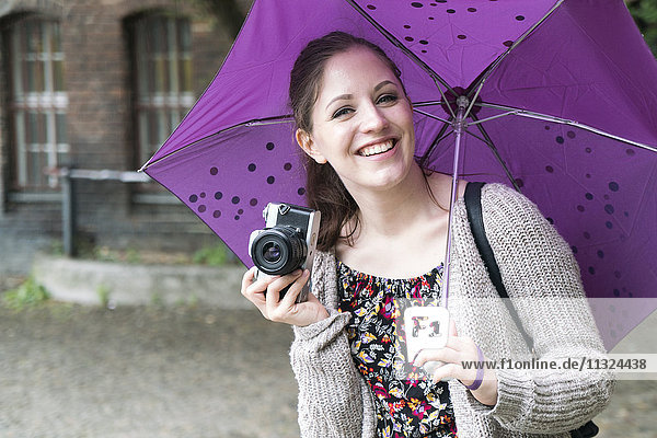 Fröhliche junge Frau mit Kamera und Regenschirm Outddors