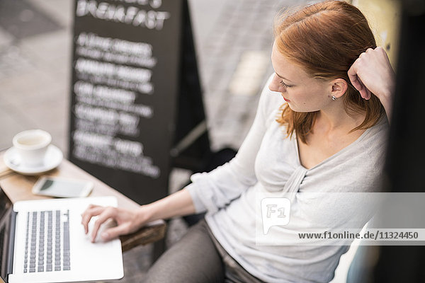 Redheaded woman using laptop at sidewalk cafe