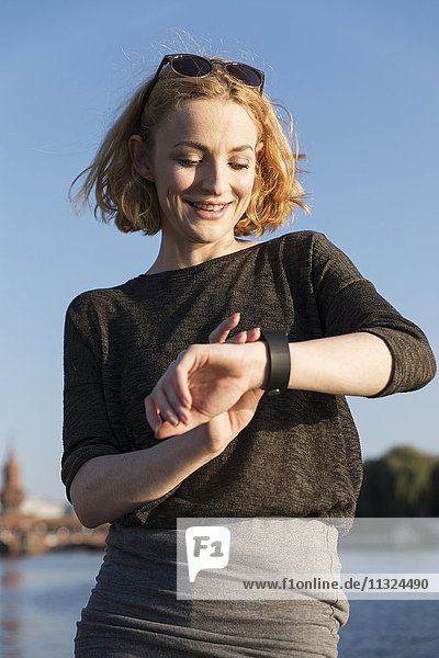 Lächelnde junge Frau überprüft ihre Smartwatch