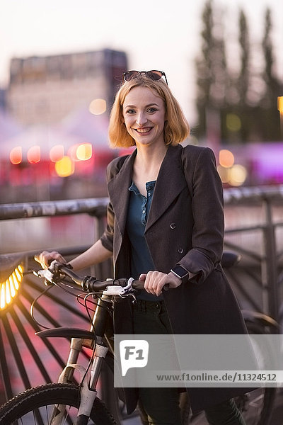 Porträt einer glücklichen jungen Frau mit Fahrrad in der Abenddämmerung