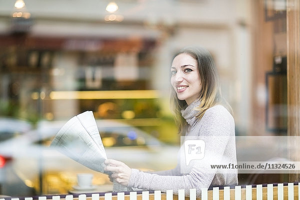 Junge Frau sitzt im Café und liest Zeitung.