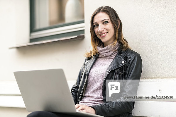 Junge Frau sitzend auf der Außenbank mit Laptop
