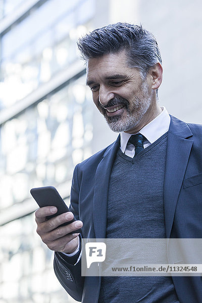 Lächelnder Geschäftsmann im Freien mit Blick aufs Handy