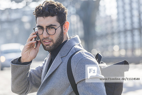 Portrait of young businessman with backpack on the phone