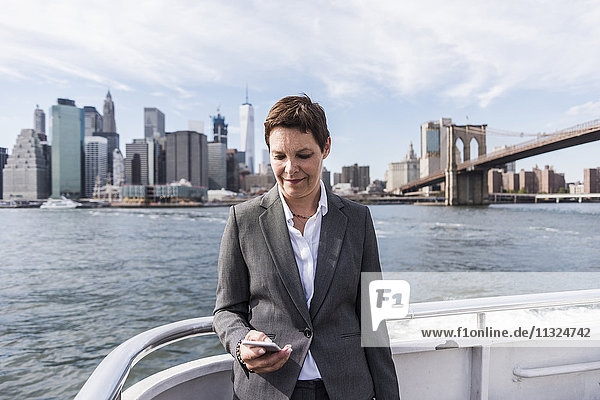 USA  Brooklyn  Porträt einer Geschäftsfrau  die auf dem Boot steht und das Handy ansieht.