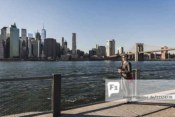 USA  Brooklyn  Geschäftsfrau mit Kopfhörer mit Blick auf die Skyline von Manhattan