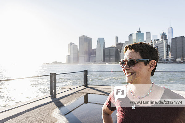 USA  Brooklyn  Porträt einer lächelnden Frau mit Sonnenbrille vor der Skyline von Manhattan
