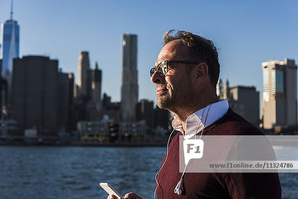 USA  Brooklyn  Geschäftsmann mit Smartphone und Kopfhörer bei Sonnenlicht