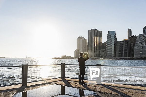 USA  Brooklyn  Rückansicht des Mannes  der die Skyline von Manhattan mit Tablette fotografiert.