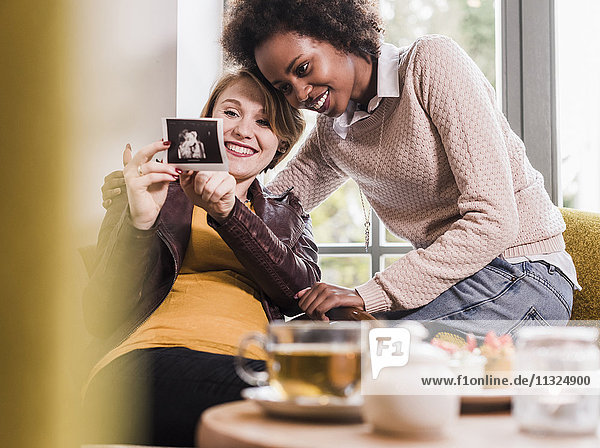 Eine schwangere junge Frau zeigt einem Freund in einem Café einen Ultraschall.