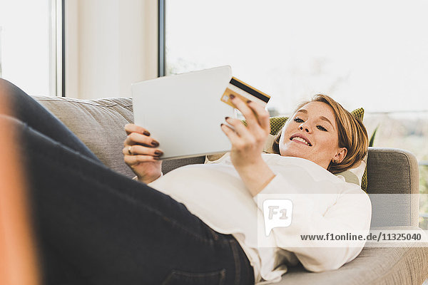 Lächelnde schwangere Frau auf der Couch online einkaufen