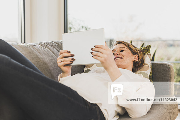 Smiling pregnant woman on couch holding tablet