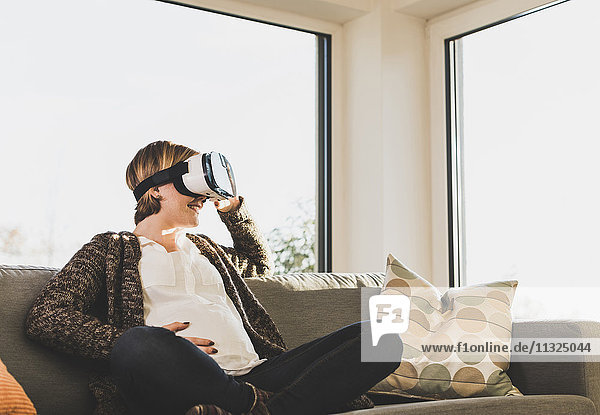Schwangere auf der Couch mit VR-Brille