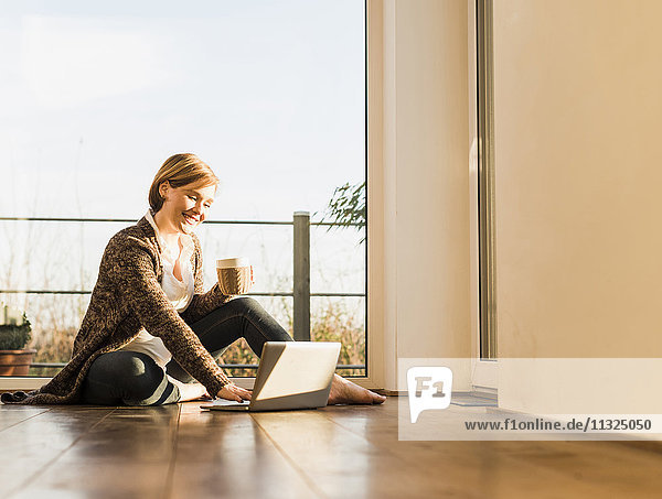 Smiling pregnant woman sitting on floor using laptop
