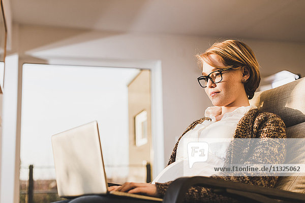Pregnant woman sitting in armchair using laptop