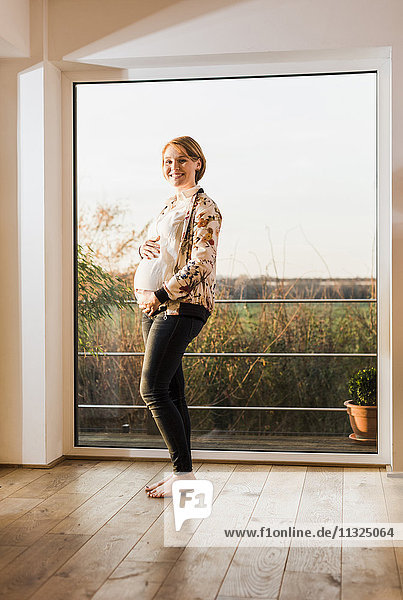 Schwangere Frau am Fenster stehend