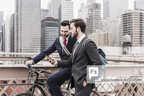 USA  New York City  two businessmen with bicycle and cell phone on Brooklyn Bridge