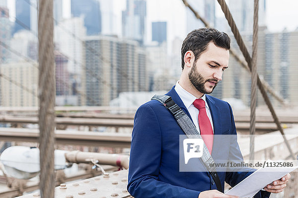 USA  New York City  businessman on Brooklyn Bridge reading document