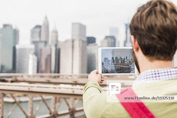 USA  New York City  Mann auf der Brooklyn Bridge beim Fotografieren von Tabletten